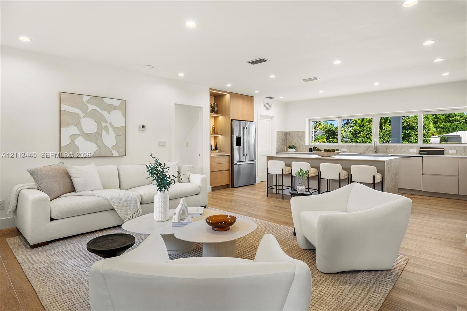 Open-concept kitchen featuring an expansive center island, integrated cabinetry, stainless steel appliances, and wood-finish flooring illuminated by r
