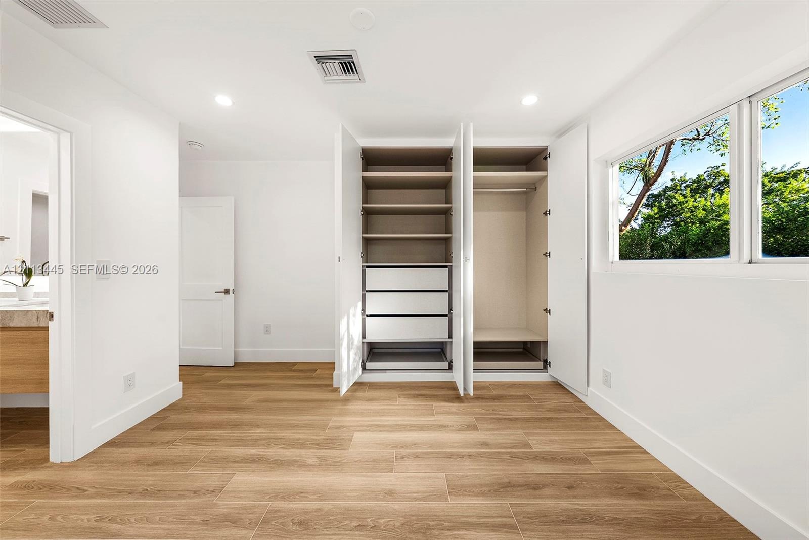Built-in wardrobe featuring integrated shelving, pull-out drawers, and hanging rods, complemented by wood-finish flooring and recessed lighting
