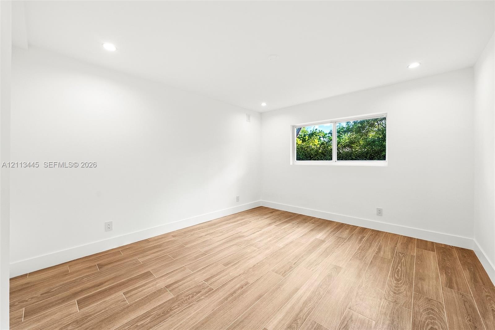 Bright room featuring wood-finish flooring, crisp white wall finishes, recessed lighting, and a window with exterior greenery