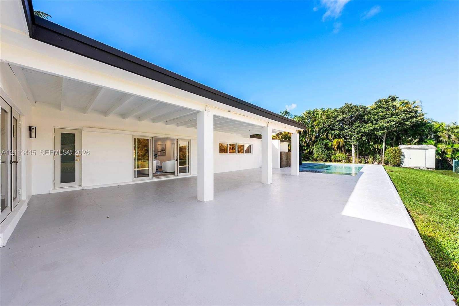 Covered patio featuring an expansive concrete surface, support columns, sliding glass doors, a built-in swimming pool, and a manicured lawn