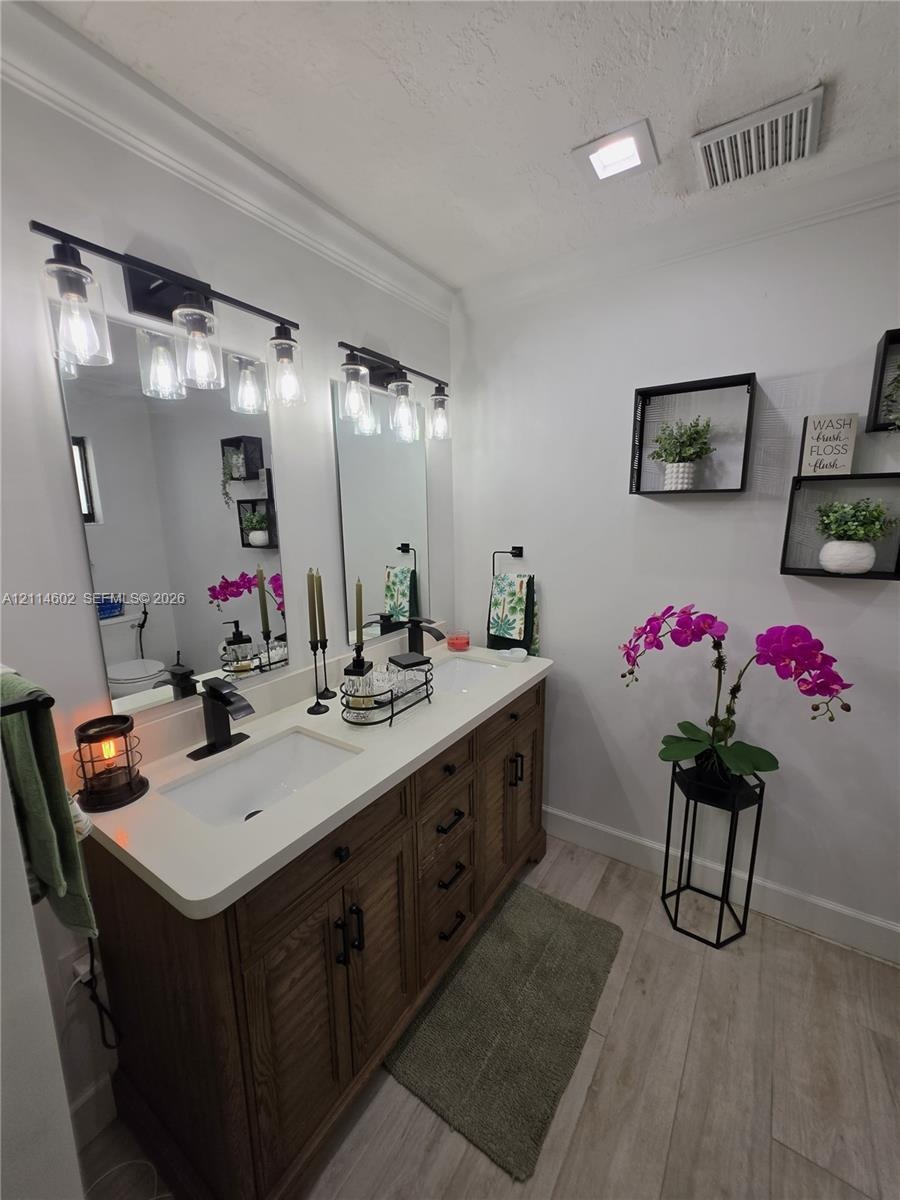 Double vanity featuring a light-toned countertop, dual rectangular undermount sinks, wood-finish cabinetry, matte black hardware, and two industrial-s