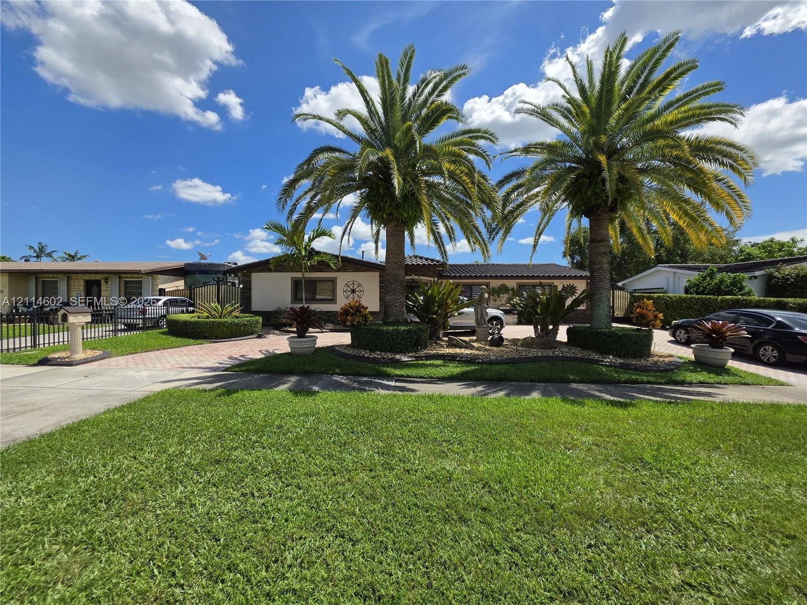 Single-story exterior featuring a paver driveway, mature palm trees, professional landscaping, and a manicured lawn