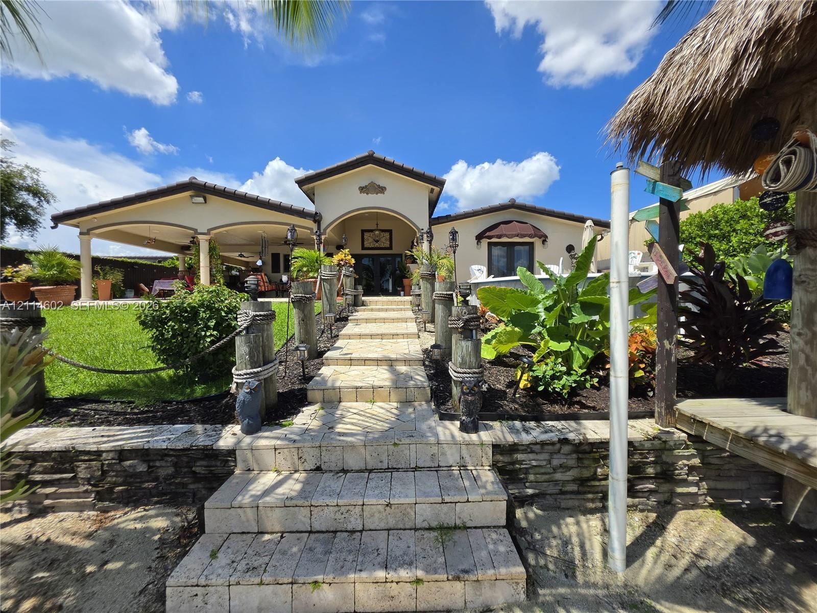Stone walkway with wood pilings and rope railing, covered patio with arched supports, and tiered stone retaining wall