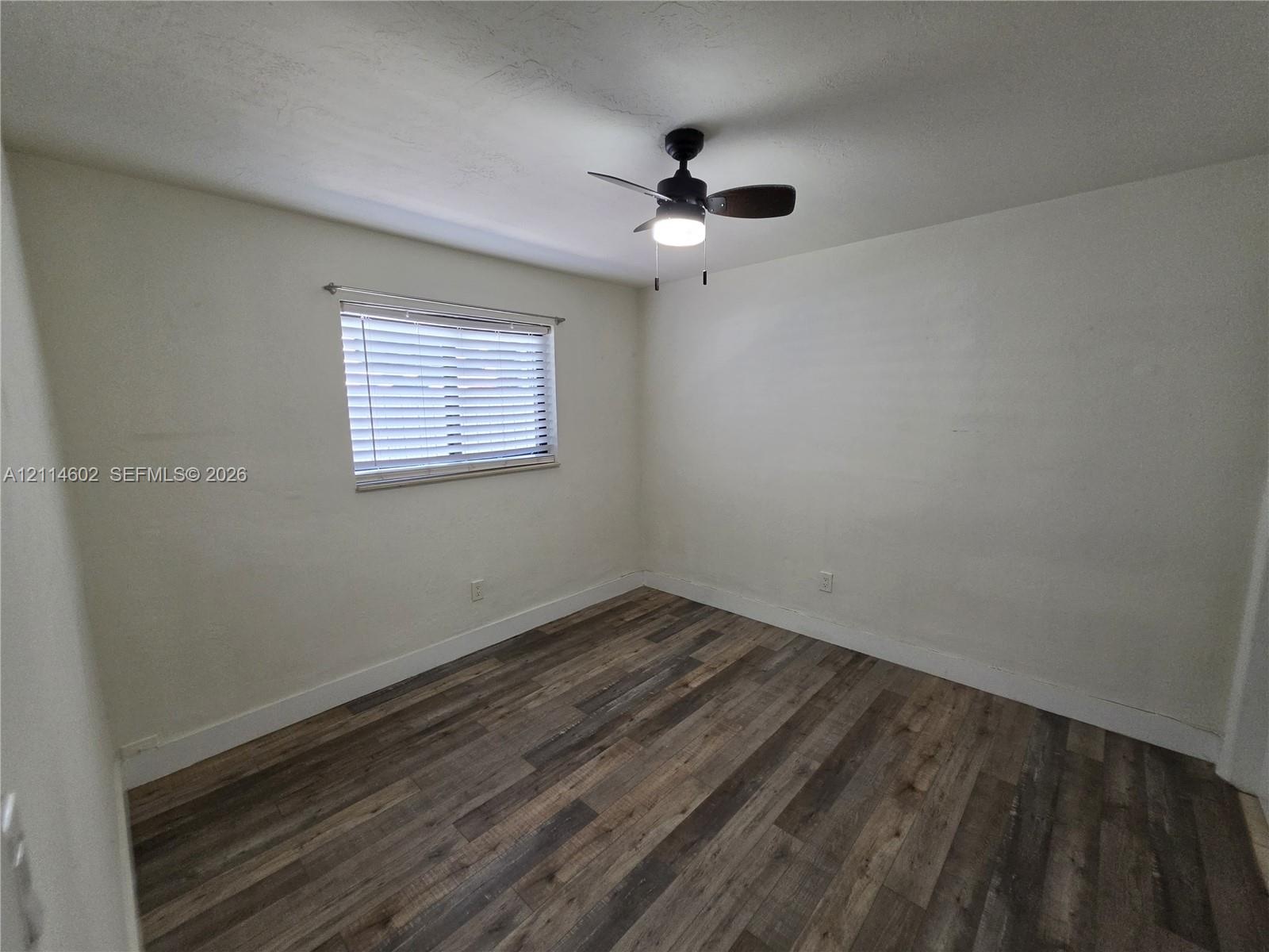 Interior room featuring wood-finish flooring, a neutral wall palette, a single window with horizontal blinds, and a ceiling-mounted fan with light fix