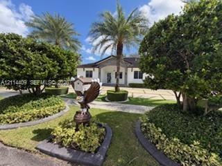 Exterior facade featuring a paved driveway, manicured landscaping, stone garden borders, and mature palm trees