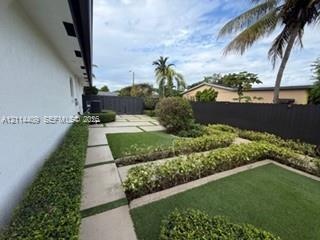 Landscaped backyard featuring tiered turf lawn sections, linear concrete pavers, structured hedge borders, and a privacy fence