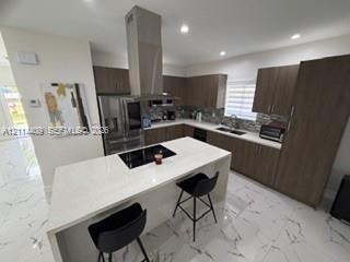 Kitchen featuring a central island with a quartz countertop and integrated cooktop, stainless steel chimney-style range hood, wood-finish cabinetry, s