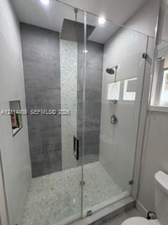 Walk-in shower featuring a frameless glass enclosure, ceiling-mounted rainfall showerhead, pebble stone floor, vertical mosaic tile accent, and a buil