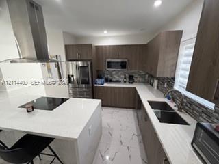 Kitchen featuring wood-finish cabinetry, quartz countertops, a central island with a built-in cooktop, stainless steel chimney-style range hood, and t