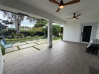 Covered patio featuring wood-finish tile flooring, dual ceiling fans, and an outdoor living area with stone paver hardscaping and integrated turf