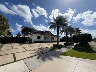 Single-story residence featuring a white stucco exterior, expansive paver driveway with turf accents, arched entryway, and mature palm trees