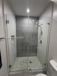 Walk-in shower featuring a glass enclosure, gray tile surround, pebble-style floor, built-in recessed niche, and handheld shower fixture