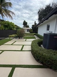 Backyard featuring large-format paver hardscaping with turf ribbons, perimeter privacy fencing, manicured hedges, and an external storage structure