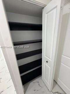 Storage closet featuring white paneled swing doors, multiple horizontal shelving tiers with dark-toned surfaces, and large-format tile flooring with v