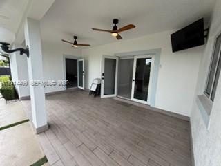 Covered patio featuring wood-finish tile flooring, dual ceiling fans, wall-mounted television, and glass-paneled exterior doors