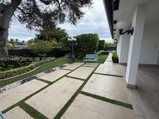 Covered patio featuring wood-finish flooring, large-format concrete pavers with turf inlays, professional landscaping, and wall-mounted exterior light
