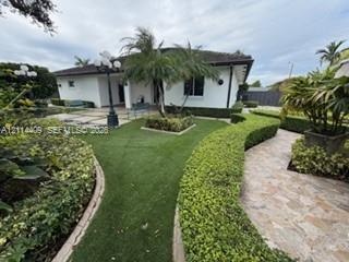 Landscaped exterior grounds featuring a paved walkway, manicured hedging, synthetic turf, and hardscaped patio area