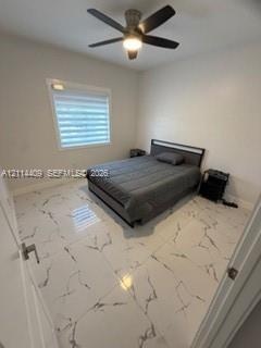 Large-format tile flooring with veined detailing, neutral wall tones, multi-blade ceiling fan with integrated lighting, and horizontal shade window tr