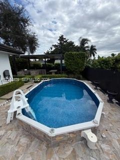 Oval swimming pool with tile-surfaced exterior, stone-paver decking, and a covered outdoor structure featuring built-in masonry elements