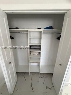 Walk-in closet featuring white-finish built-in shelving, two overhead storage ledges, metal hanging rods, and large-format tile flooring with a veined