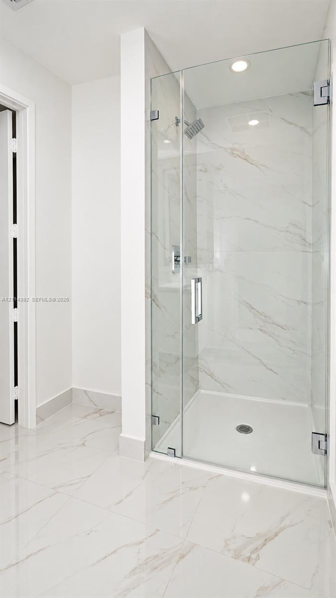 Walk-in shower featuring glass enclosure, wall-mounted rainfall showerhead, and large-format tile flooring and wall surfacing with veined detailing