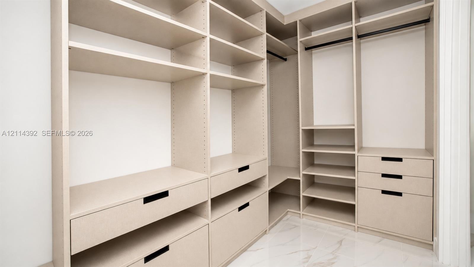 Custom walk-in closet featuring extensive built-in shelving, multiple integrated drawers with matte black pulls, dual hanging rods, and stone-finish f