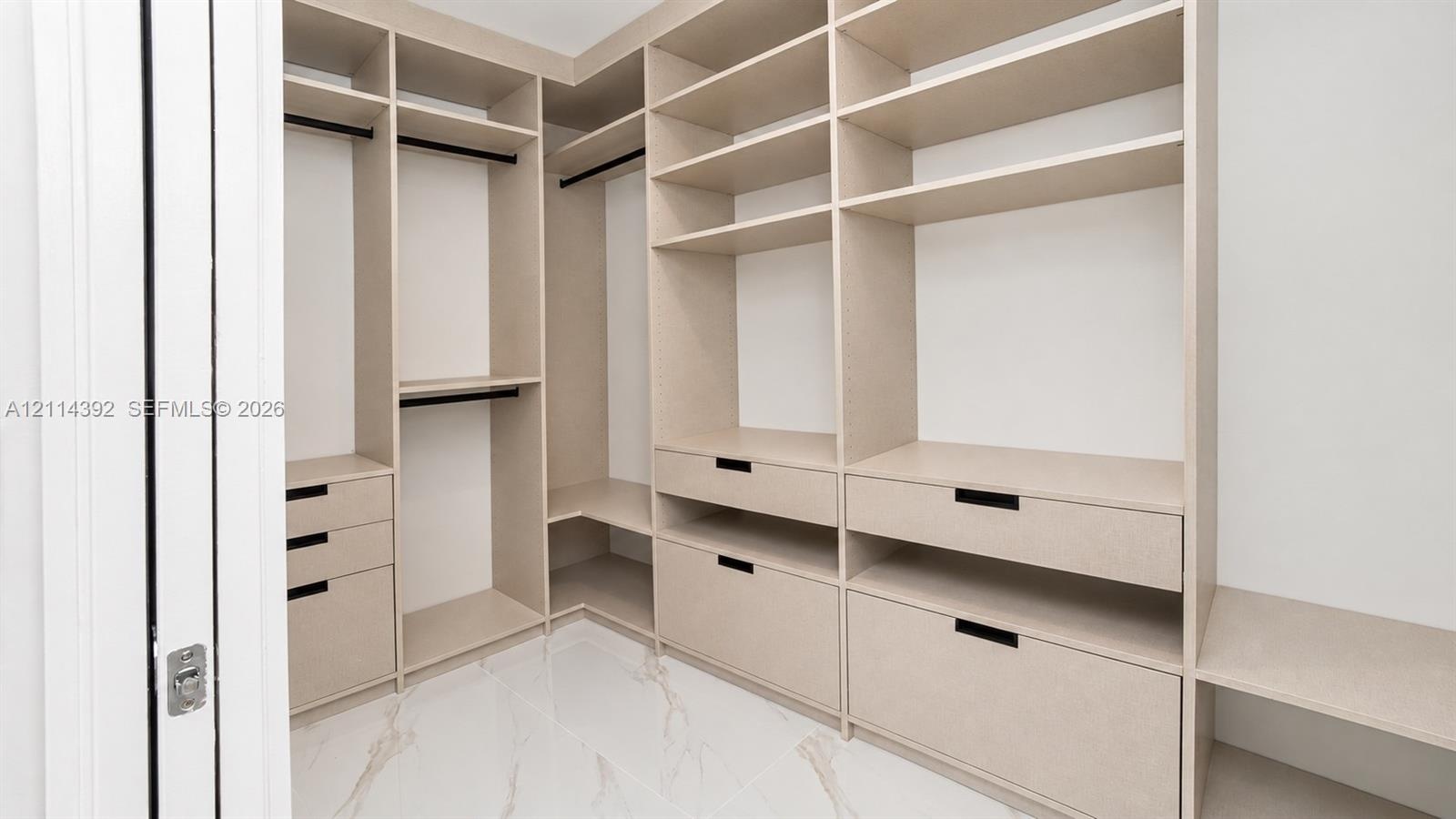 Custom walk-in closet featuring extensive built-in shelving, integrated storage drawers, hanging rods, and large-format tile flooring