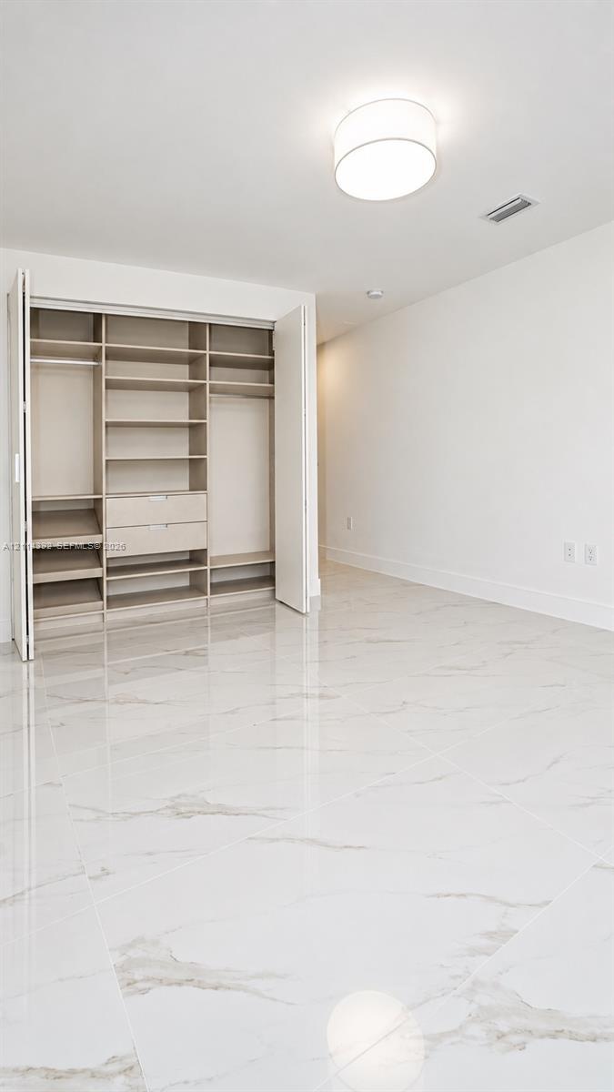 Large-format white tile flooring with veining, built-in closet organization system with integrated drawers and shelving, and flush-mount drum ceiling 