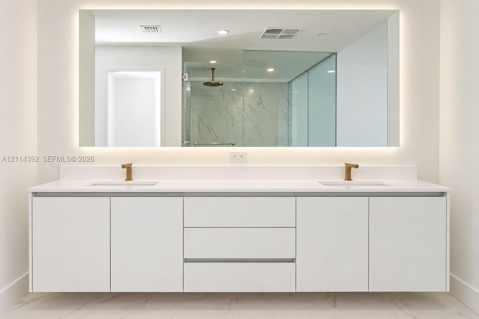 Floating white dual-sink vanity with a solid surface countertop, metallic finish faucets, a large rectangular mirror with integrated perimeter lightin