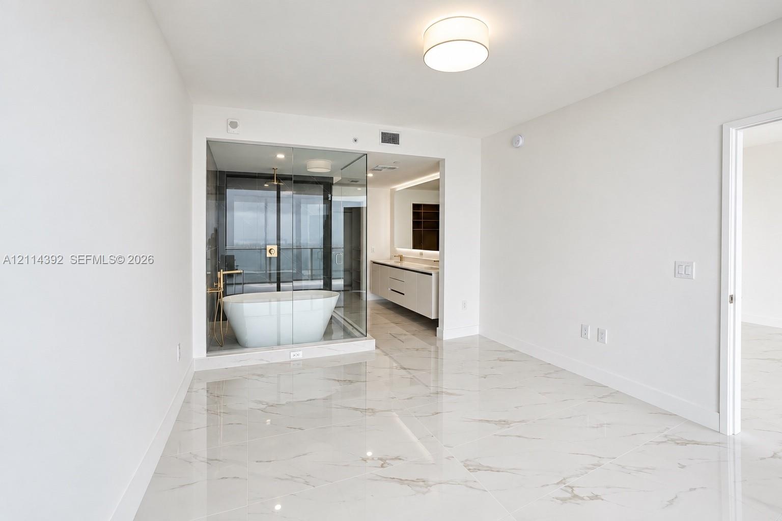 Polished stone-finish flooring, glass-enclosed bathroom area featuring a freestanding soaking tub, dual-sink floating vanity, and flush-mount lighting