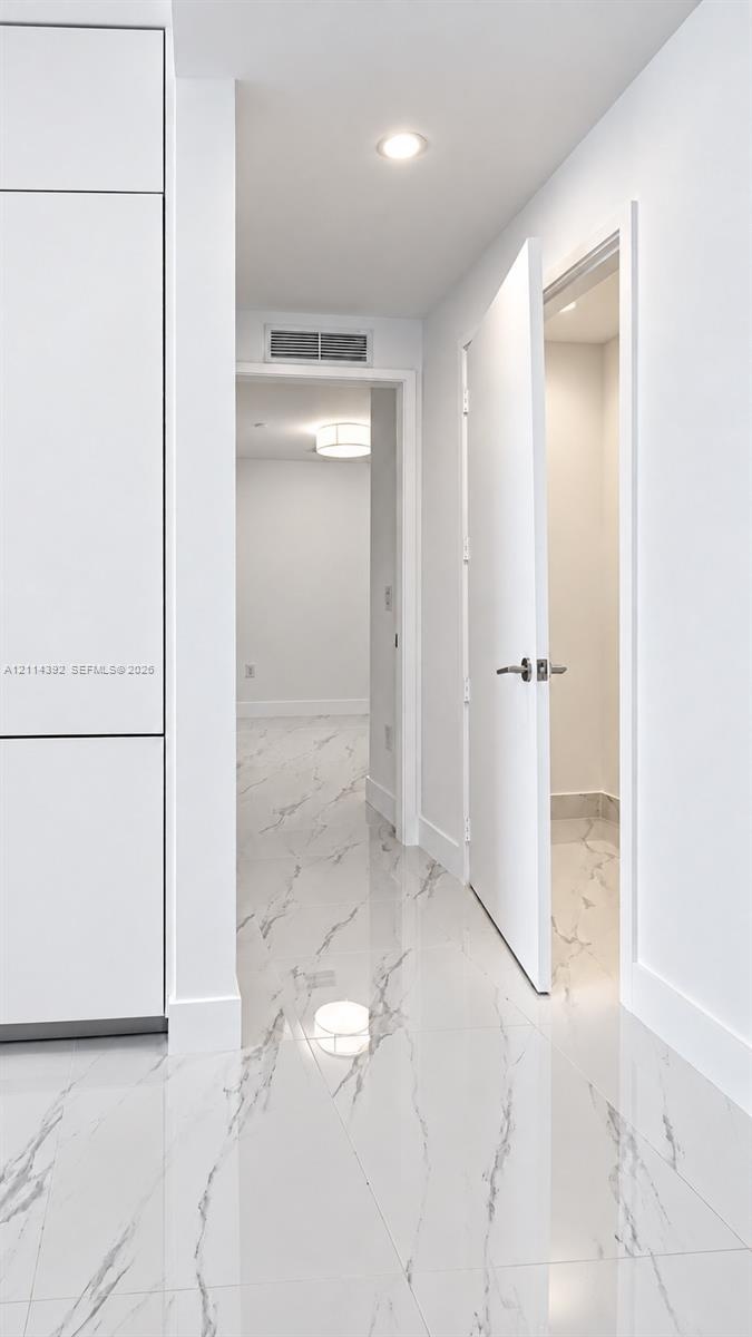 Polished stone-finish flooring with marbled detailing, full-height built-in cabinetry, recessed ceiling lighting, and solid-core interior doors with m