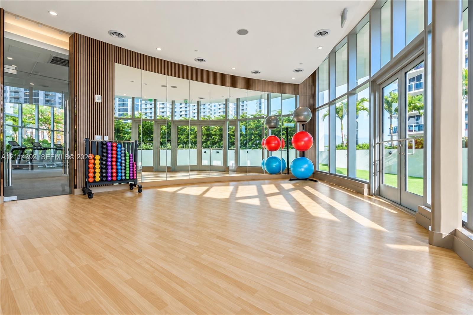 Fitness studio featuring floor-to-ceiling glass walls, wood-finish flooring, full-length mirror wall, and wood slat accent wall
