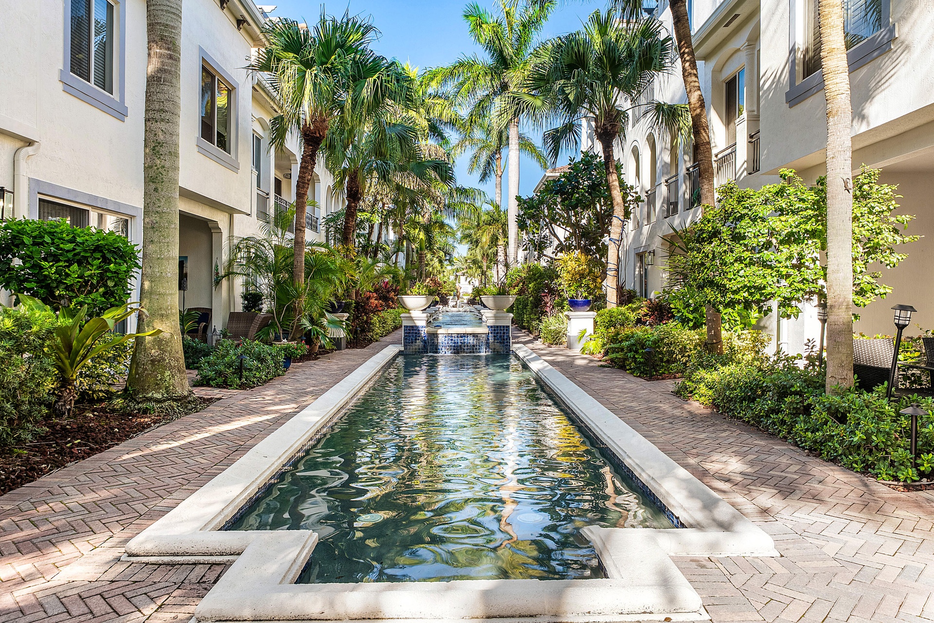 Elongated water feature with tiered fountain, surrounded by mature palm trees and lush landscaping