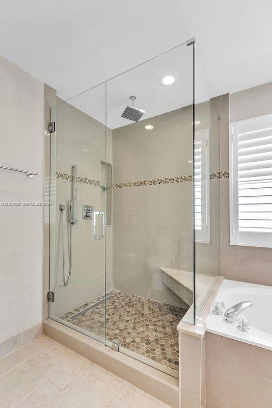 Walk-in shower featuring a frameless glass enclosure, rainfall showerhead, handheld sprayer, built-in corner bench, and mosaic tile flooring with deco