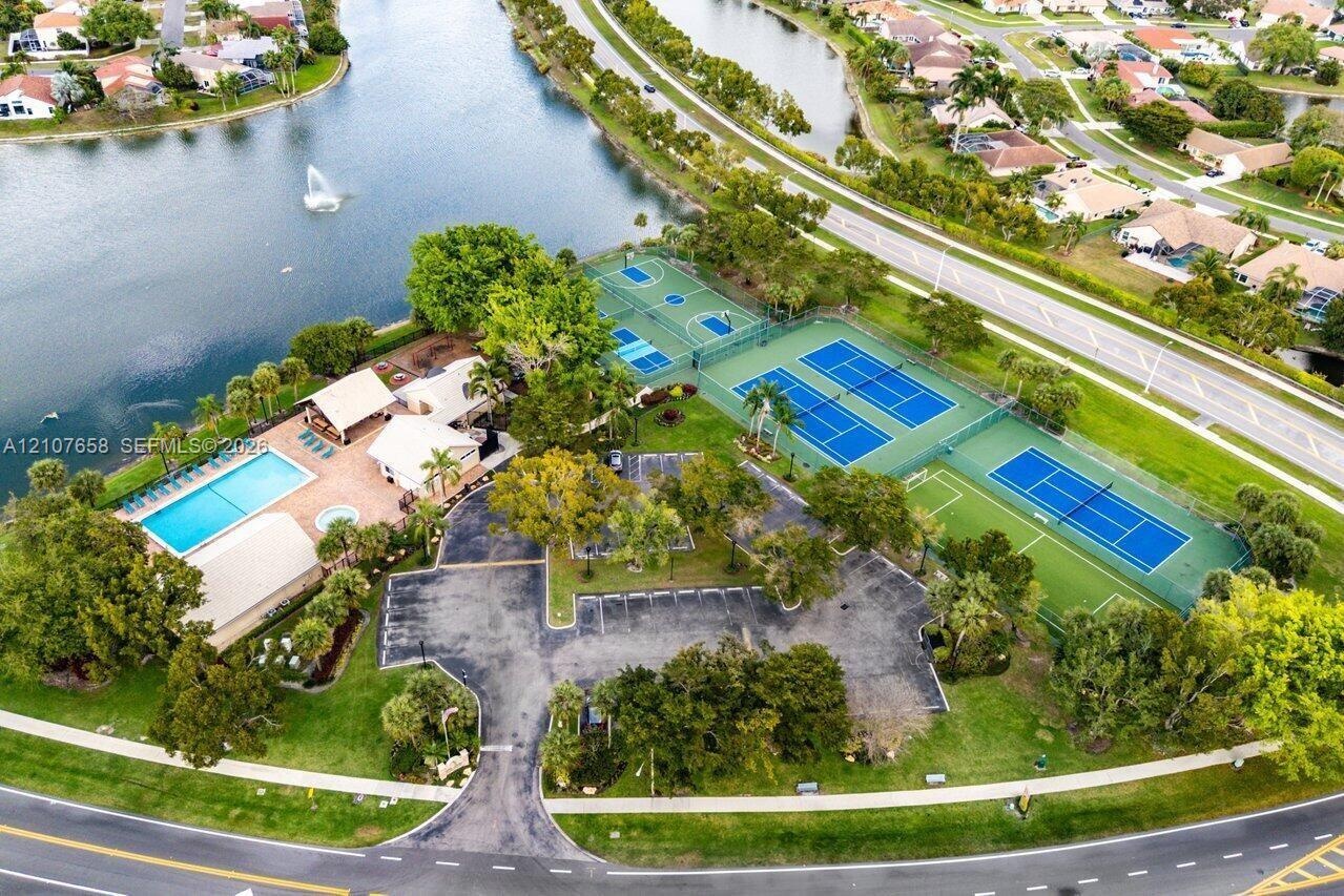 Recreational facility featuring a swimming pool, multiple tennis courts, a basketball court, and paved parking area situated on a waterfront lot