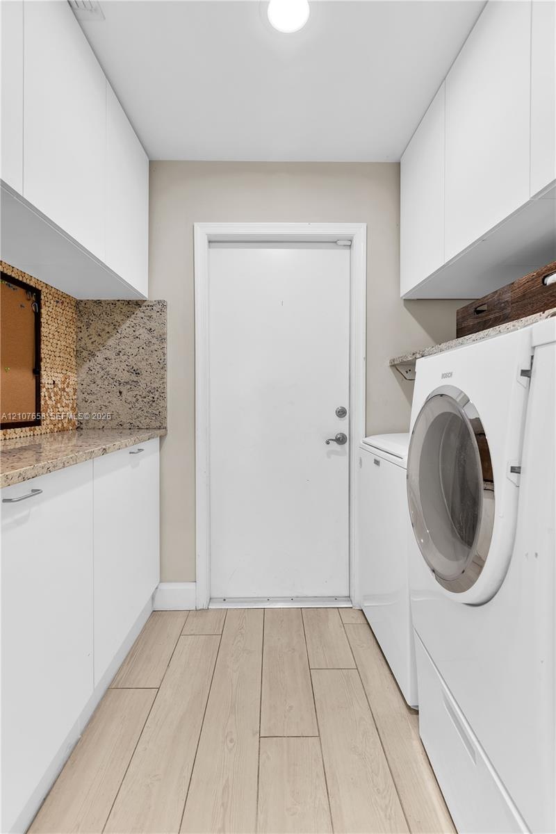 Utility room featuring wood-finish flooring, white flat-panel upper and lower cabinetry, stone-finish countertops, and a decorative mosaic tile backsp