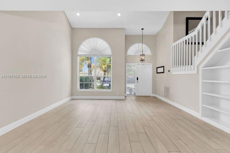 Vaulted ceiling featuring arched windows, wood-finish flooring, built-in shelving, and a decorative pendant light