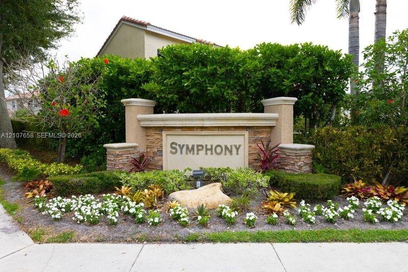 Community monument sign featuring stone veneer accents, stucco columns, and professionally landscaped flower beds