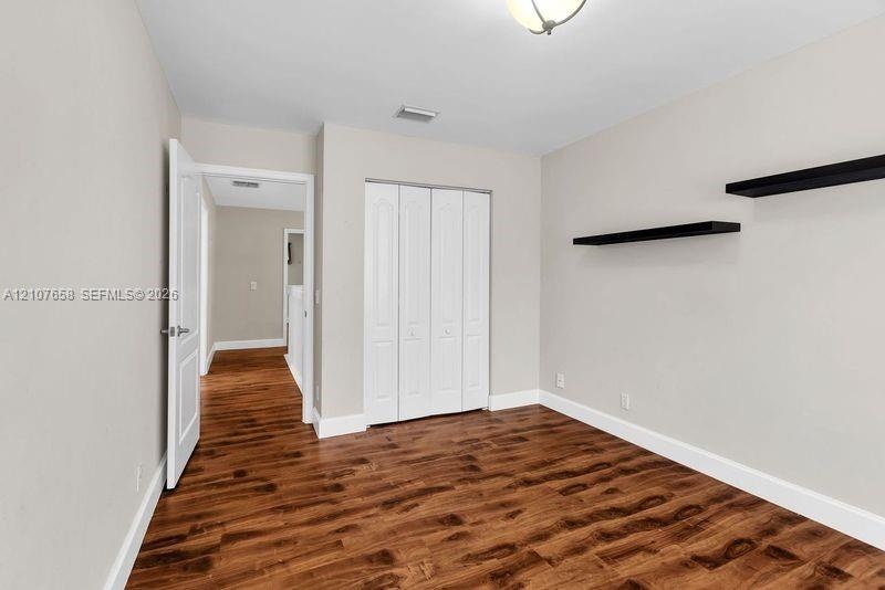 Room featuring wood-finish flooring, bi-fold closet doors, and wall-mounted shelving
