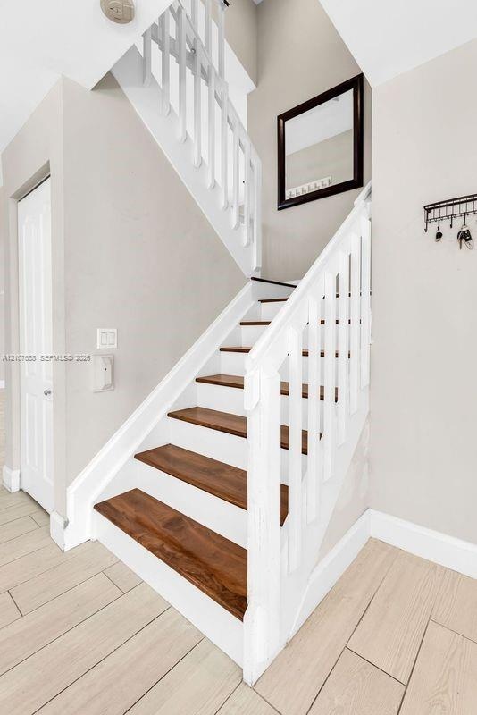 Staircase featuring white balusters and railings with dark wood-finish treads, complemented by light wood-finish flooring