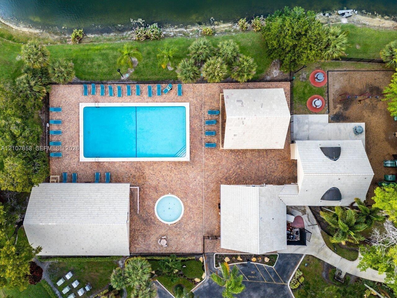 Aerial perspective of community facilities featuring a rectangular swimming pool, a circular spa, brick-paver decking, and pitched-roof structures