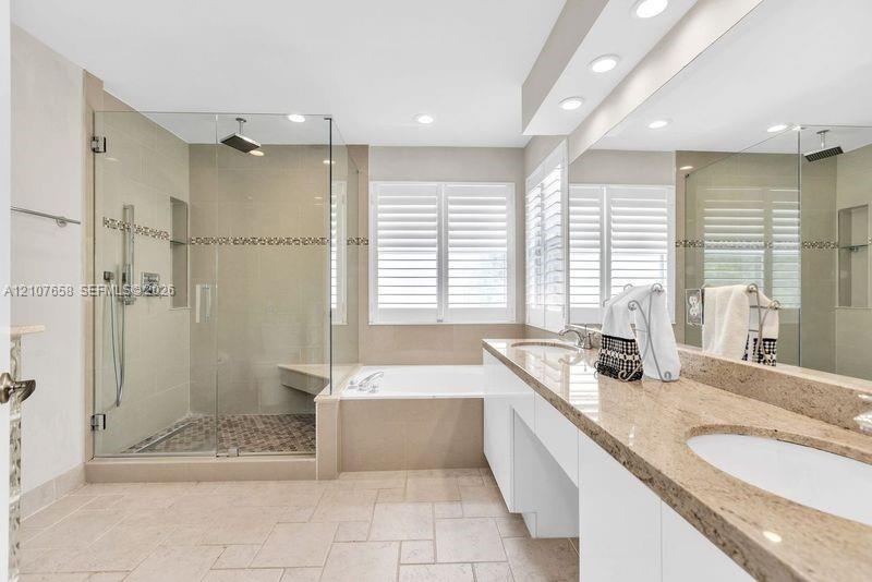 Bathroom featuring a dual-sink vanity with stone countertops, a glass-enclosed walk-in shower with a tiled bench and pebble-style flooring, a deep soa