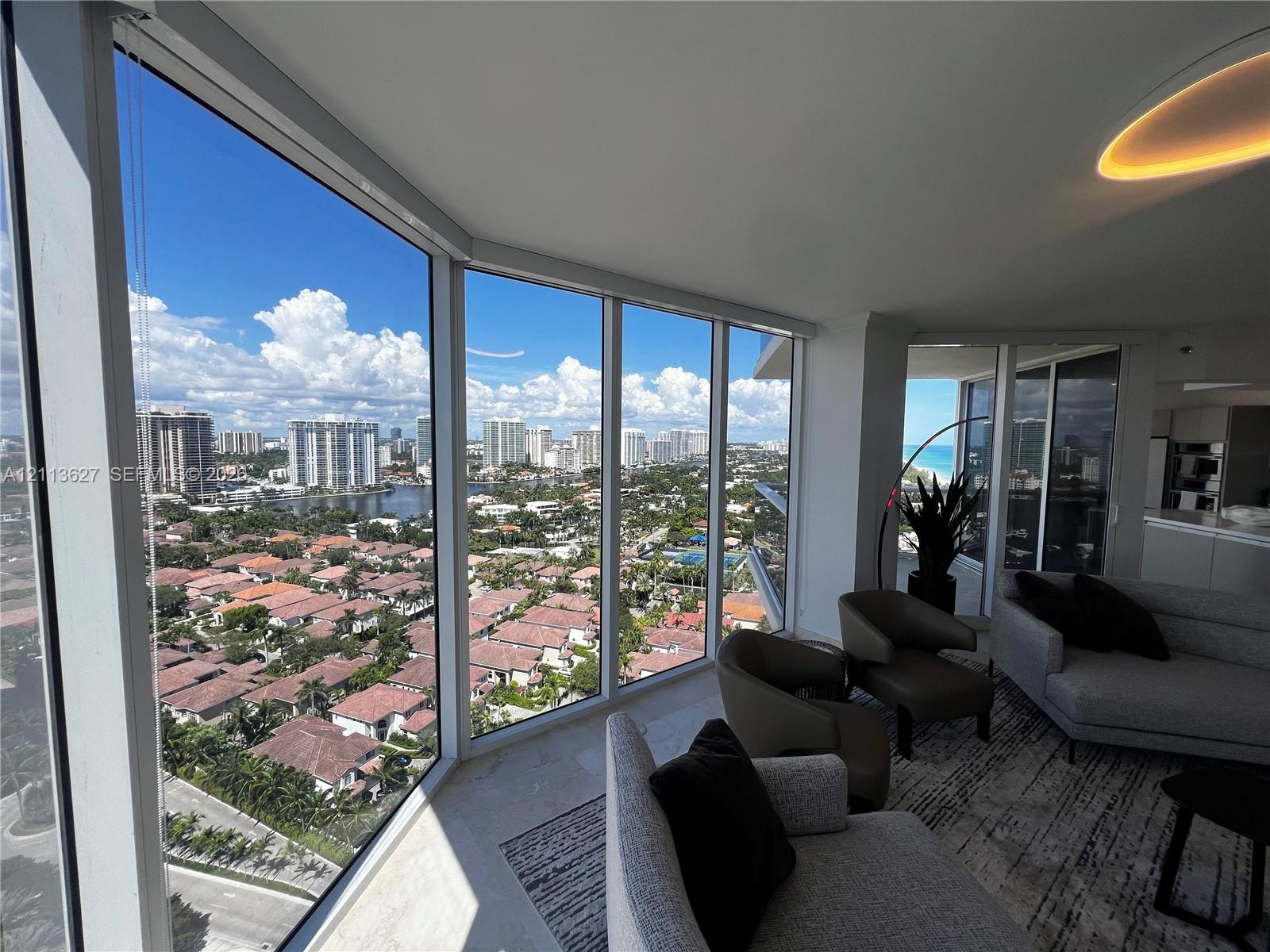 Floor-to-ceiling windows featuring panoramic urban and coastal scenery, neutral tile flooring, and integrated recessed ceiling lighting