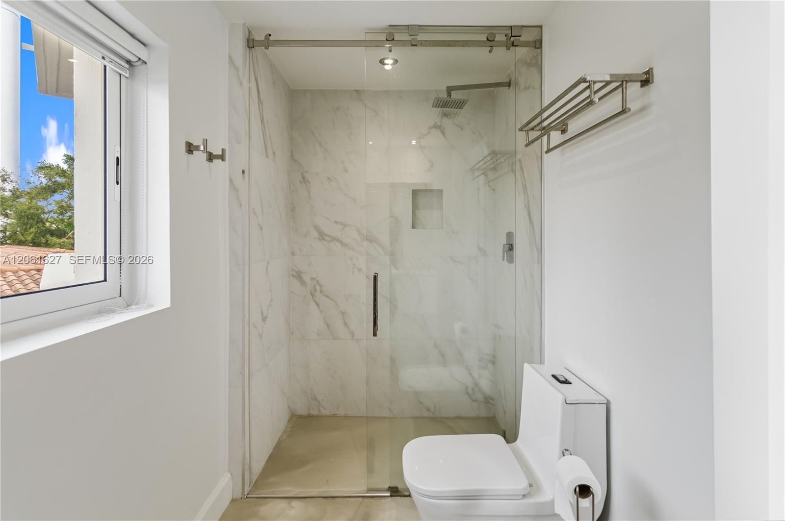Walk-in shower featuring glass sliding doors, stone-patterned wall tile, built-in recessed niche, and an overhead rainfall showerhead
