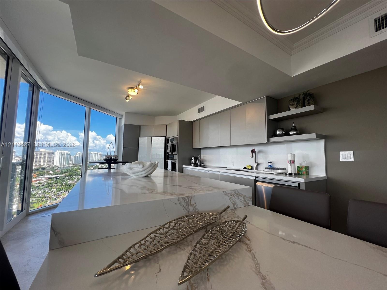 Kitchen featuring a waterfall-edge island with stone-finish countertop, flat-panel cabinetry, open shelving, integrated stainless steel appliances, an