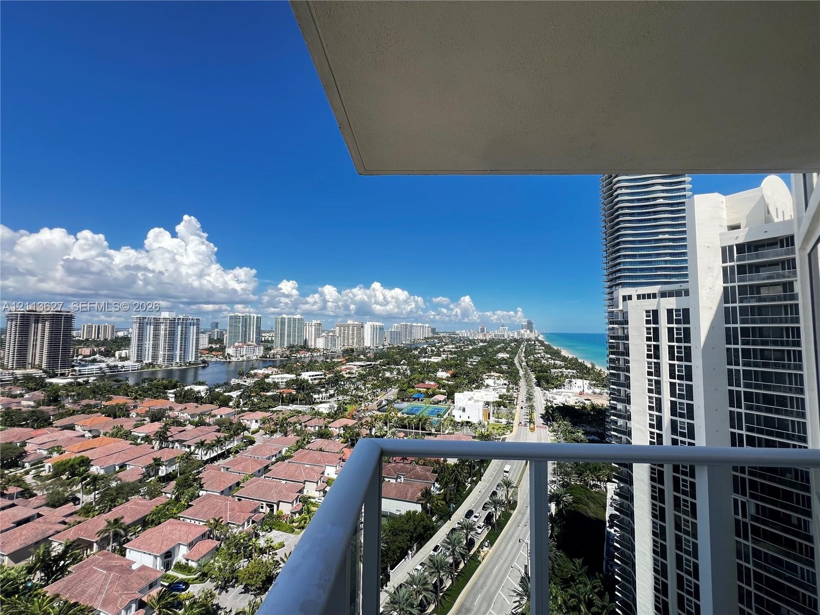 Private balcony featuring a glass-panel railing and panoramic coastal and urban scenery