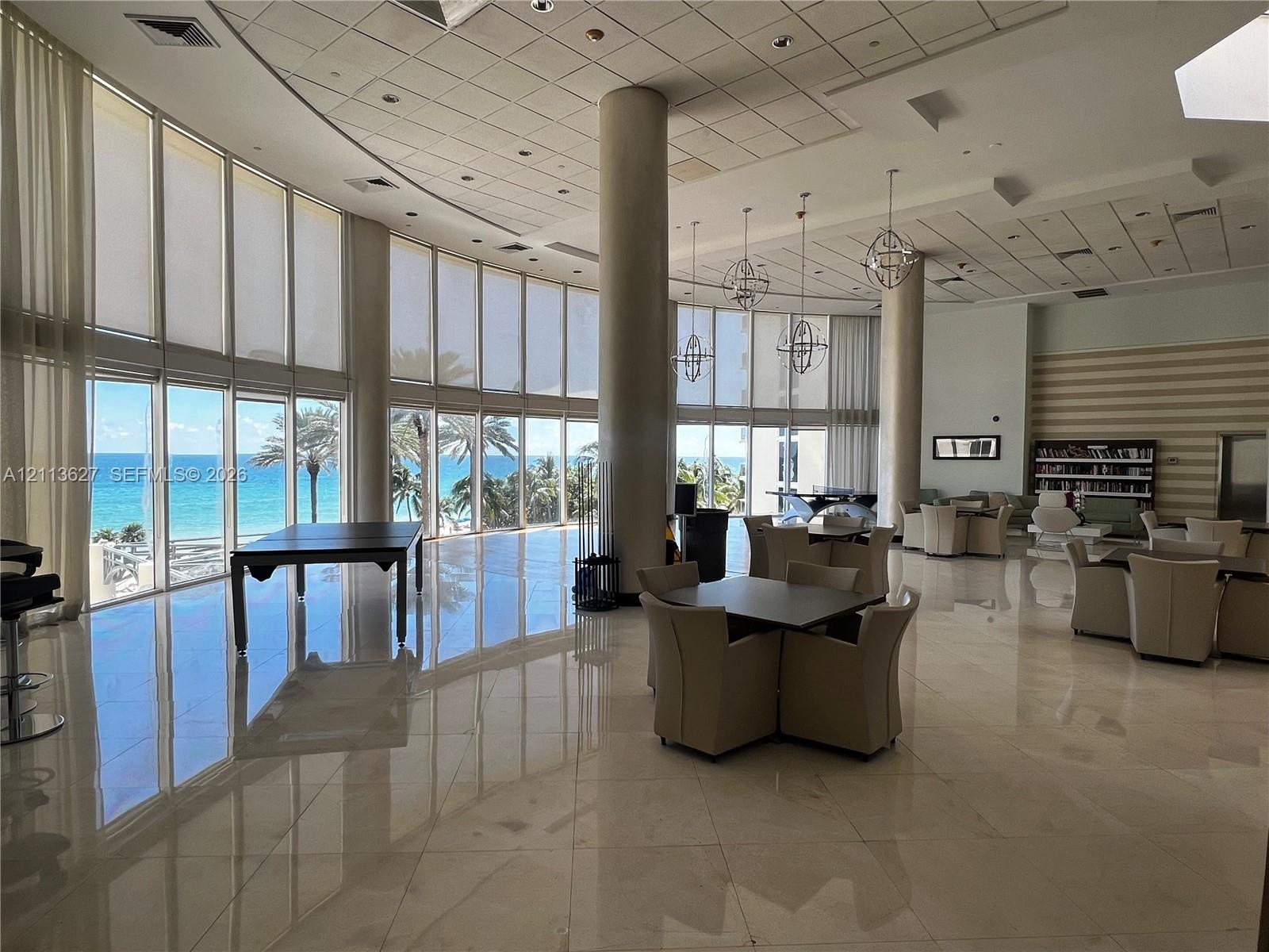 Expansive common area featuring floor-to-ceiling windows, polished stone flooring, structural columns, and spherical pendant lighting, with direct exp