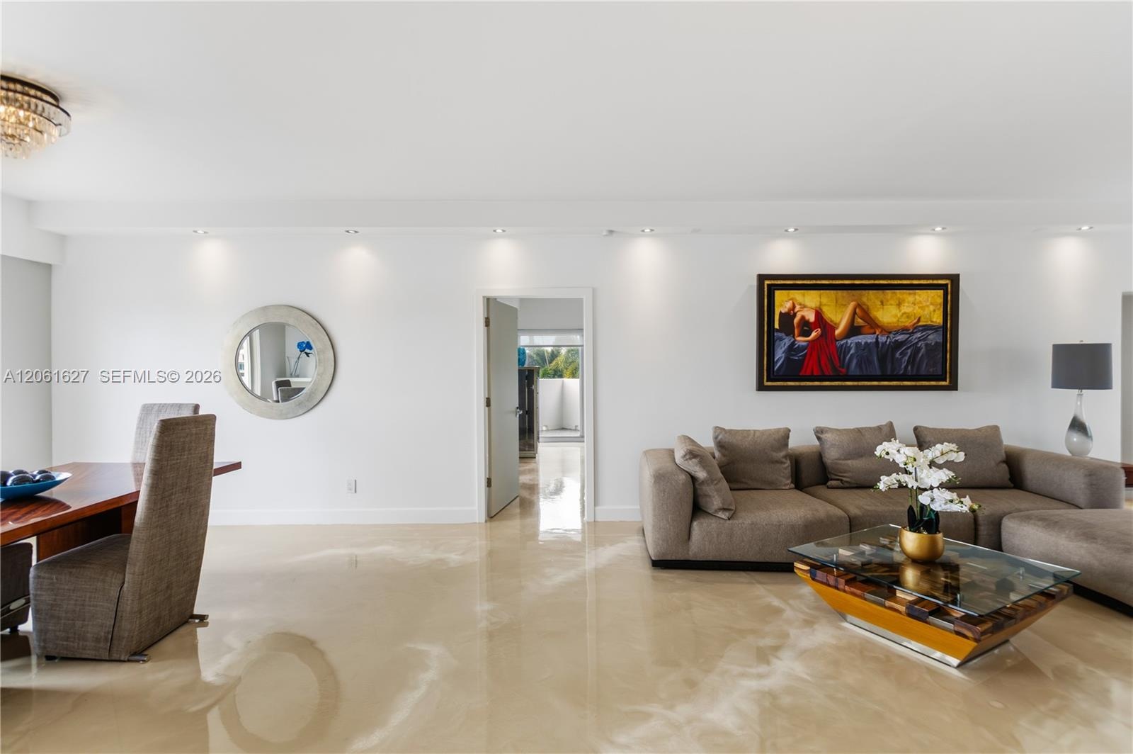 Open-concept interior featuring large-format polished flooring, recessed ceiling lighting, a crystal flush-mount light fixture, and a circular wall mi