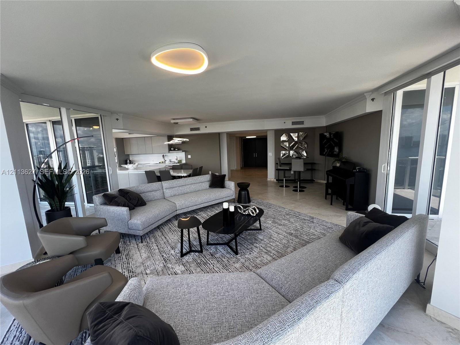 Open-concept living area featuring stone-finish flooring, floor-to-ceiling glass panel doors, custom recessed ceiling lighting, and minimalist built-i