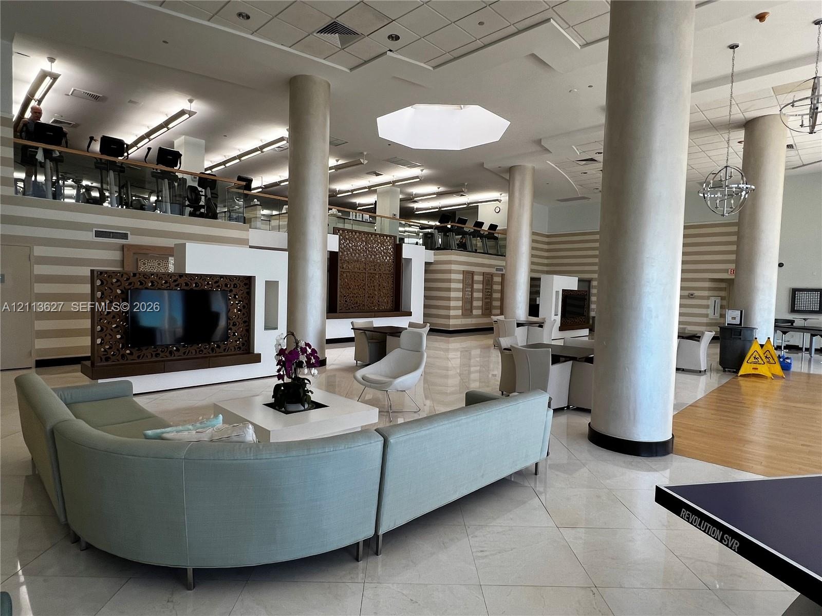 Spacious common area featuring large structural columns, polished stone flooring, intricate laser-cut wood privacy screens, and overhead geometric lig